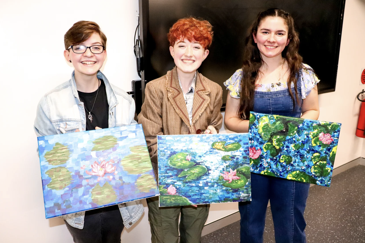 Three teenagers hold up paintings of waterlilies